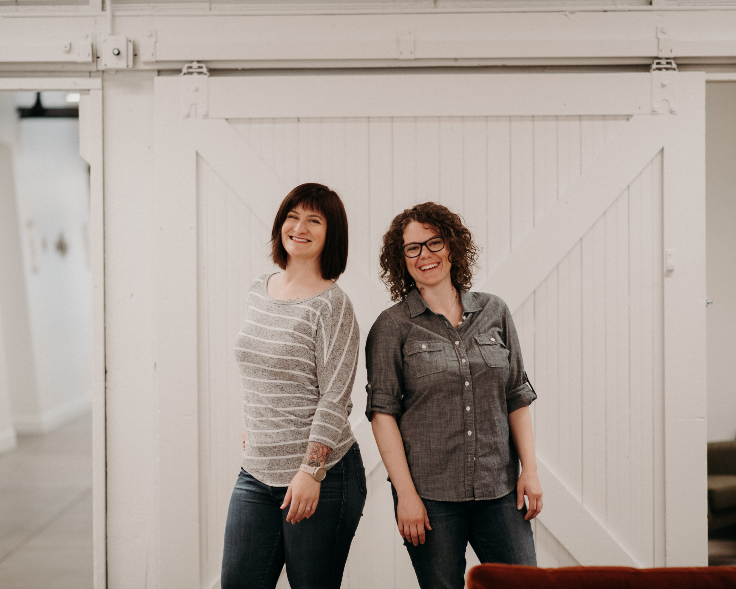 Madison and Brandi standing together in front of a white barn door, smiling.