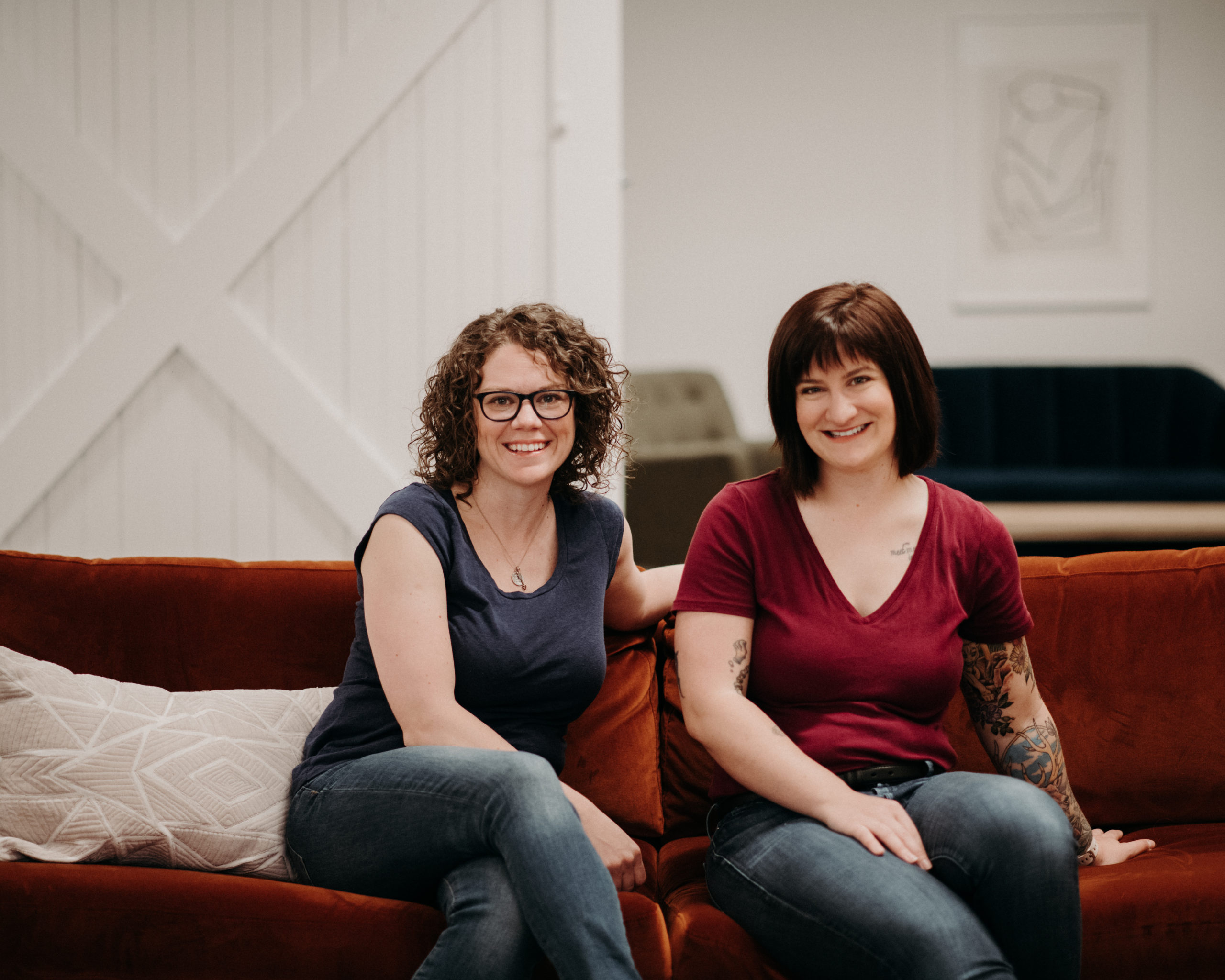 Madison and Brandi sitting together on a red couch, smiling.